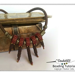 Puede incluir: Un collar de cuentas con un cordón de cuero marrón y cuentas rojas y marrones. El collar se muestra en una caja de madera con un cierre de latón. La imagen incluye el texto "Studio183 Beading Tutorial Copyright Heather Collin".