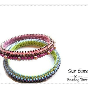 Op de afbeelding: Twee kralenarmbanden, een bovenop de andere. De bovenste armband is bruin, roze en groen. De onderste armband is blauw, groen en bruin. De armbanden worden "Star Gazer" genoemd en zijn een kralenworkshop.