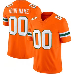 Puede incluir: Dos camisetas de fútbol naranja con números blancos y detalles verdes. Una camiseta muestra "YOUR NAME" encima del número "00". La otra camiseta también tiene el número "00" en la parte delantera. Ambas camisetas tienen rayas verdes y blancas en las mangas.