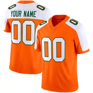 Puede incluir: Dos camisetas de fútbol naranja con detalles blancos y verdes. Las camisetas tienen el número "00" en la parte delantera y trasera, con el texto "YOUR NAME" en la espalda. Las camisetas tienen un diseño de cuello en V.