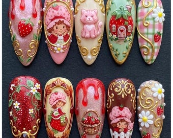 May include: A set of ten almond-shaped press-on nails featuring intricate 3D designs including strawberry motifs, a character in a strawberry hat, a pink cat, a strawberry-shaped house, a basket of strawberries, and gold filigree accents.