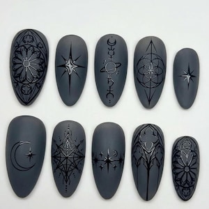 May include: A set of ten gray, almond-shaped false nails with intricate black designs. The designs include celestial symbols, geometric patterns, and gothic-style motifs. The nails are arranged in two rows of five.