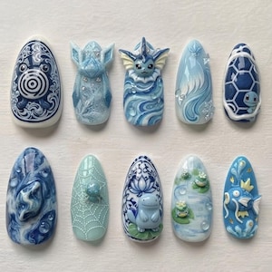 Peut inclure: Un ensemble de dix faux ongles présentant des motifs bleus et blancs inspirés par des créatures aquatiques et des thèmes marins. Chaque ongle affiche des détails sculptés en 3D, incluant des personnages, des volutes et des motifs floraux.