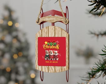 May include: A wooden Christmas ornament shaped like a sled, with red metal runners and a rope for hanging. The ornament features a red square with the words "Merry Christmas" and three corgis wearing holiday sweaters. The text "Peace, Joy, and Love" is also included.