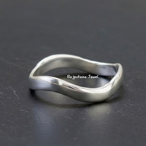 May include: A silver-colored ring with a wavy design. The ring has a smooth, polished surface and a simple, elegant style. The text "Rajputana Jewel" is visible on the ring.