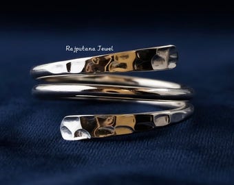 May include: A silver-toned bypass ring featuring a multi-coil design with a hammered, textured finish on the outer ends. The metal surface reflects light, and the text Rajputana Jewel is printed in white above the ring on a dark blue background.