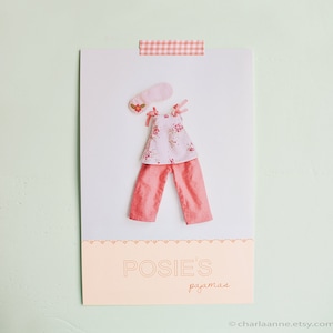 May include: A pink and white floral print pajama top and pink pants with a pink eye mask. The text "POSIES pajamas" is printed on the bottom of the card.
