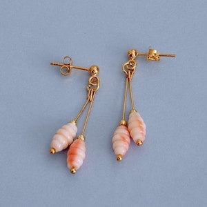 May include: A pair of gold-colored dangle earrings. Each earring features a post, a small gold bead, and a delicate gold wire suspending two coral-colored, ridged beads. The beads have a gradient of pink and white.