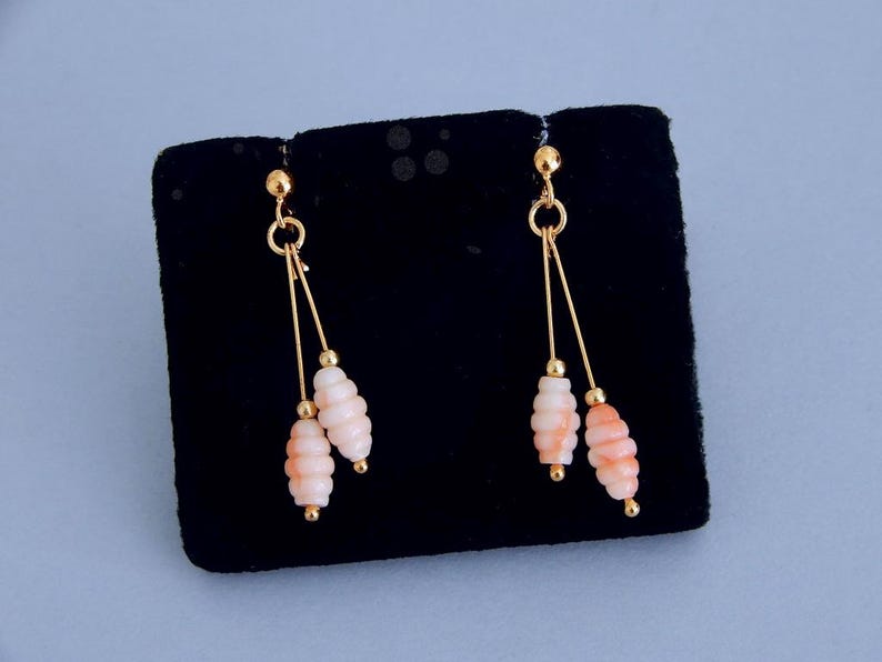 May include: A pair of gold-toned earrings with a delicate design. Each earring features a small gold ball at the top, connected to a slender gold wire. Two strands of gold wire suspend a cluster of light pink, textured beads.