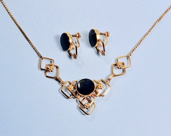Pode incluir: Um colar de ouro com um pingente de pedra preta e brincos combinando. O colar apresenta um design geométrico com formas quadradas.