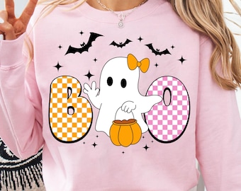 Könnte beinhalten: Hellrosa Sweatshirt mit einem Halloween-Motiv. Das Design beinhaltet das Wort "BOO" mit einem Geistercharakter, Fledermäusen, Sternen und einem Kürbis. Die Buchstaben "B" und "O" haben ein kariertes Muster in Orange und Rosa.