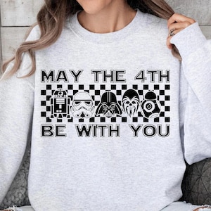Puede incluir: Sudadera gris claro con el texto "MAY THE 4TH BE WITH YOU" en letras negras. Debajo del texto hay un patrón de cuadros blancos y negros con gráficos de personajes de Star Wars.
