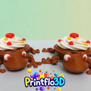 May include: Two brown frog-shaped cupcake holders with white frosting, red and yellow sprinkles. The frog's eyes are red. The Printflo3D logo is in the bottom right corner.
