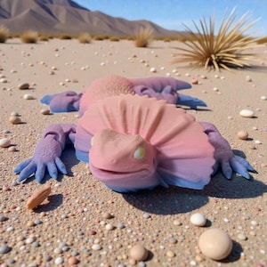 Könnte beinhalten: Eine 3D-gedruckte Eidechsenfigur in Rosa-, Lila- und Blautönen, die auf einer sandigen Oberfläche mit kleinen Kieselsteinen liegt. Die Eidechse hat einen Kragen um den Kopf. Der Hintergrund zeigt eine Wüstenlandschaft.
