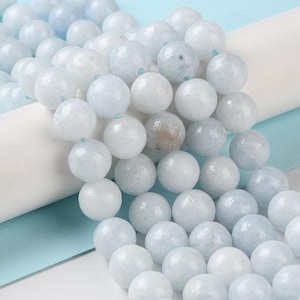 May include: Close-up of a strand of round, light blue and white beads. The beads have a smooth, polished surface and are strung together with a light blue thread. The beads are a mix of opaque white and translucent blue.
