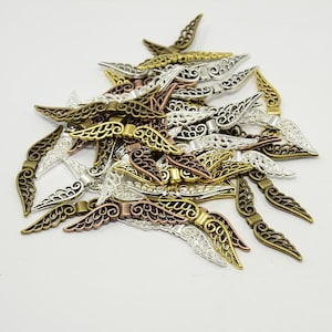 May include: A collection of filigree wing-shaped metal charms in various metallic finishes, including gold, silver, bronze, and copper. The charms have intricate openwork designs and are suitable for jewelry making or craft projects.
