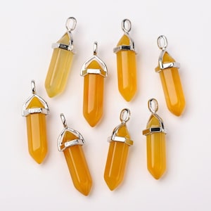 Peut inclure: Un ensemble de huit pendentifs en cristal jaune, chacun présentant une forme pointue hexagonale lisse surmontée d'une bélière en métal argenté. Les pierres sont translucides et de couleur uniforme, disposées de manière éparse.