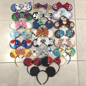 Könnte beinhalten: Eine Sammlung dekorativer Stirnbänder mit Mickey Mouse Ohren und Schleifen. Die Stirnbänder weisen Designs mit Charaktermotiven und Glitzerakzente auf. Farben sind Rot, Blau, Rosa und Gold. Einige Stirnbänder haben Text. Für dekorative Zwecke.