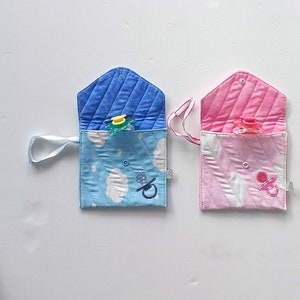 May include: Two fabric pouches with a white cloud and pacifier design. One pouch is blue and the other is pink. Both pouches have a white strap.