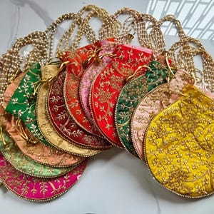 May include: A selection of embroidered drawstring bags in a range of colours, including red, green, and yellow. Each bag has gold floral patterns and is attached to a beaded gold chain.