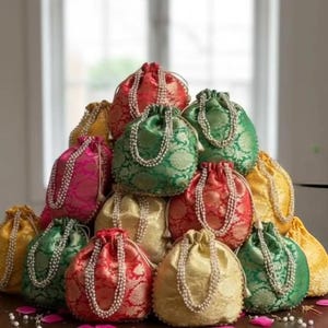 May include: A selection of vibrant drawstring bags in red, green, gold, and pink. Each bag features a pearl-like string detail around the opening. The bags are arranged in a pyramid shape, creating a visually appealing display.