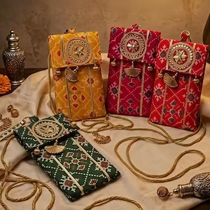 May include: Four rectangular fabric crossbody bags in yellow, dark red, bright red, and dark green. Each bag features a geometric pattern, a circular gold-toned medallion on the flap, gold-toned fan-shaped charms, and a thin gold-toned cord strap.