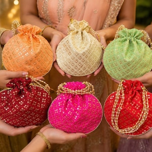 Peut inclure: Six pochettes rondes à cordon de serrage en orange, crème, vert clair, rouge foncé, rose vif et rouge vif. Chaque sac en tissu présente un motif géométrique répétitif avec broderies métalliques et sequins, fini par une anse en perles.