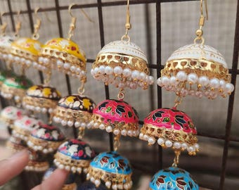 May include: A collection of multi-tiered jhumka earrings featuring bell-shaped components in various colors including white, pink, blue, and yellow. Each tier is decorated with intricate floral patterns, gold-tone metal accents, and small white beads.