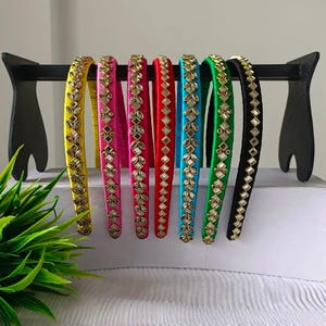 May include: A set of seven fabric-covered headbands in yellow, pink, magenta, red, blue, green, and black. Each headband features a central row of small, reflective, diamond-shaped mirror accents arranged in a repeating, intricate pattern.
