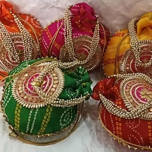 May include: A collection of five colorful, round drawstring bags. Each bag features a decorative beaded handle and a circular, ornate embellishment. The bags are in shades of orange, pink, yellow, green, and red, with gold accents.