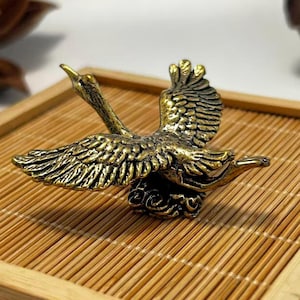 May include: A detailed brass sculpture of a swan in flight, wings outstretched. The swan is perched on a cloud-like base, with intricate feather detailing. The sculpture is set on a bamboo tray.