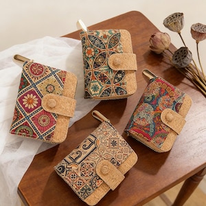 Può includere: Quattro portafogli in sughero con disegni colorati e fantasie. Ogni portafoglio ha una cerniera dorata e una chiusura con linguetta in sughero. I portafogli sono disposti su una superficie di legno, mostrando i loro motivi e le loro trame uniche.