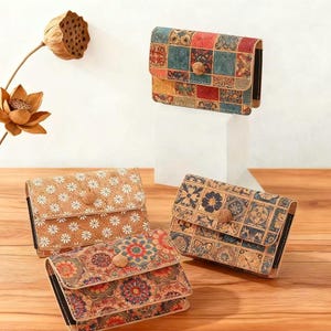 May include: Four cork wallets with different patterns are displayed on a wooden surface. The wallets feature floral, geometric, and patchwork designs in various colors. Each wallet has a button closure.