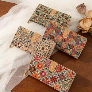 May include: Four colorful patterned wallets with cork closures and gold zippers are displayed on a wooden surface. The wallets feature intricate designs in shades of red, orange, green, and blue. The wallets are rectangular and appear to be made of a textured material.