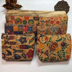 May include: A collection of cork zipper pouches with colorful floral, geometric, and fish patterns. The pouches feature silver-toned zipper pulls and are arranged on a wooden surface. The designs include red, blue, yellow, and green accents.