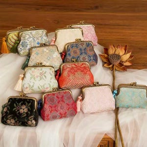 May include: A selection of small coin purses with clasp closures and tassels. The purses feature a variety of patterns and colours, including black, red, pink, blue, and cream. The designs include floral and geometric patterns.