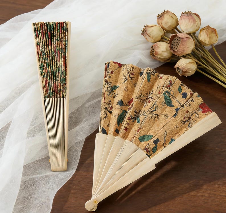 K&ouml;nnte beinhalten: Zwei dekorative Handf&auml;cher. Einer ist geschlossen und zeigt ein farbenfrohes Blumenmuster am Rand. Der andere ist ge&ouml;ffnet und zeigt einen beigen Hintergrund mit einem floralen Design in Rot, Gr&uuml;n und Blau. Beide F&auml;cher haben helle Holzgriffe.