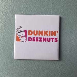 May include: A square white tile featuring a graphic logo of a coffee cup with steam and the orange text Dunkin' followed by the pink text DEEZNUTS. The design includes a small orange square behind the cup and the letters DD on the cup surface.