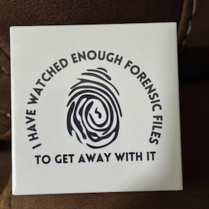 Puede incluir: Azulejo blanco cuadrado con el texto "I HAVE WATCHED ENOUGH FORENSIC FILES TO GET AWAY WITH IT" que rodea un gráfico de huella dactilar negra. El azulejo es probablemente un artículo decorativo o un posavasos.