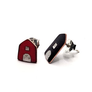 Puede incluir: Un par de pendientes de botón con diseño de granero. Un pendiente es rojo con una puerta y ventana plateadas, el otro es negro con una puerta y ventana plateadas. Los pendientes son de metal y tienen postes plateados.