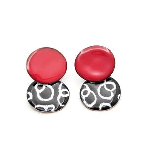 Puede incluir: Un par de pendientes rojos y negros con un patrón geométrico. Los pendientes están hechos de dos círculos, uno rojo y uno negro con un patrón blanco.