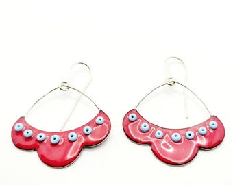May include: A pair of red enamel earrings with a scalloped edge and blue enamel beads. The earrings are silver and have a wire hook closure.