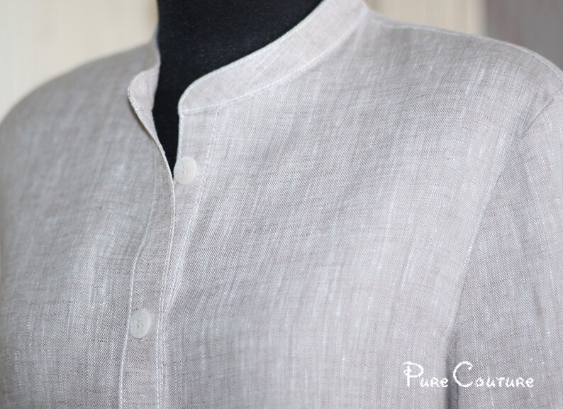 May include: A light gray linen shirt with a mandarin collar and two buttons. The shirt has a textured, woven fabric.