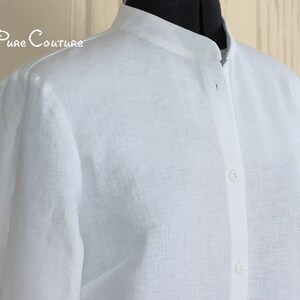 May include: A white linen shirt with a mandarin collar and long sleeves. The shirt has a button closure at the front.