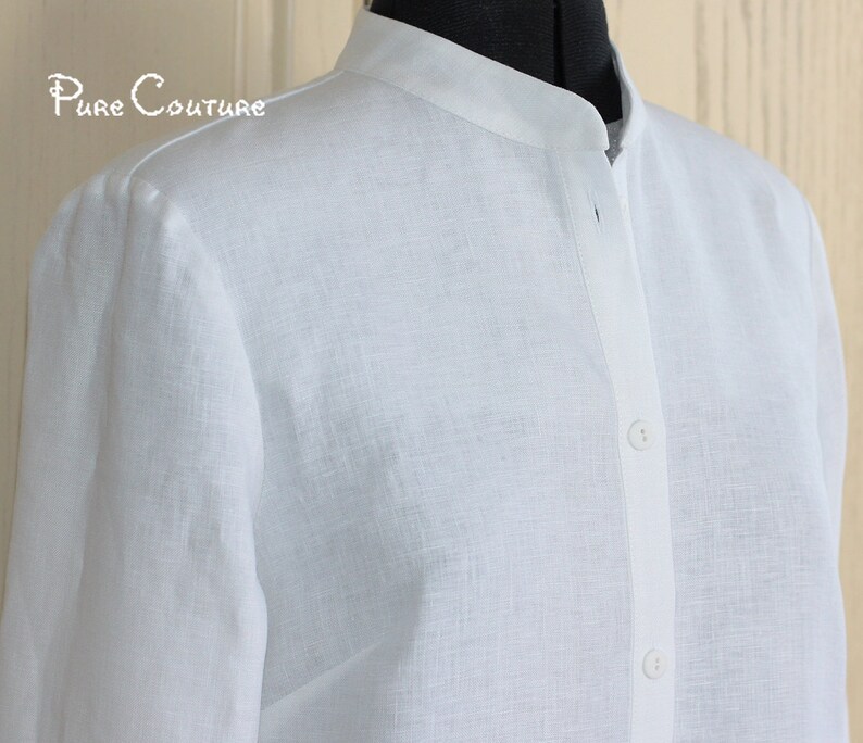 May include: A white linen shirt with a mandarin collar and long sleeves. The shirt has a button closure at the front.