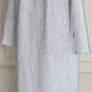 May include: A long, light gray linen shirt with a collar and long sleeves. The shirt has a subtle texture and a relaxed fit.