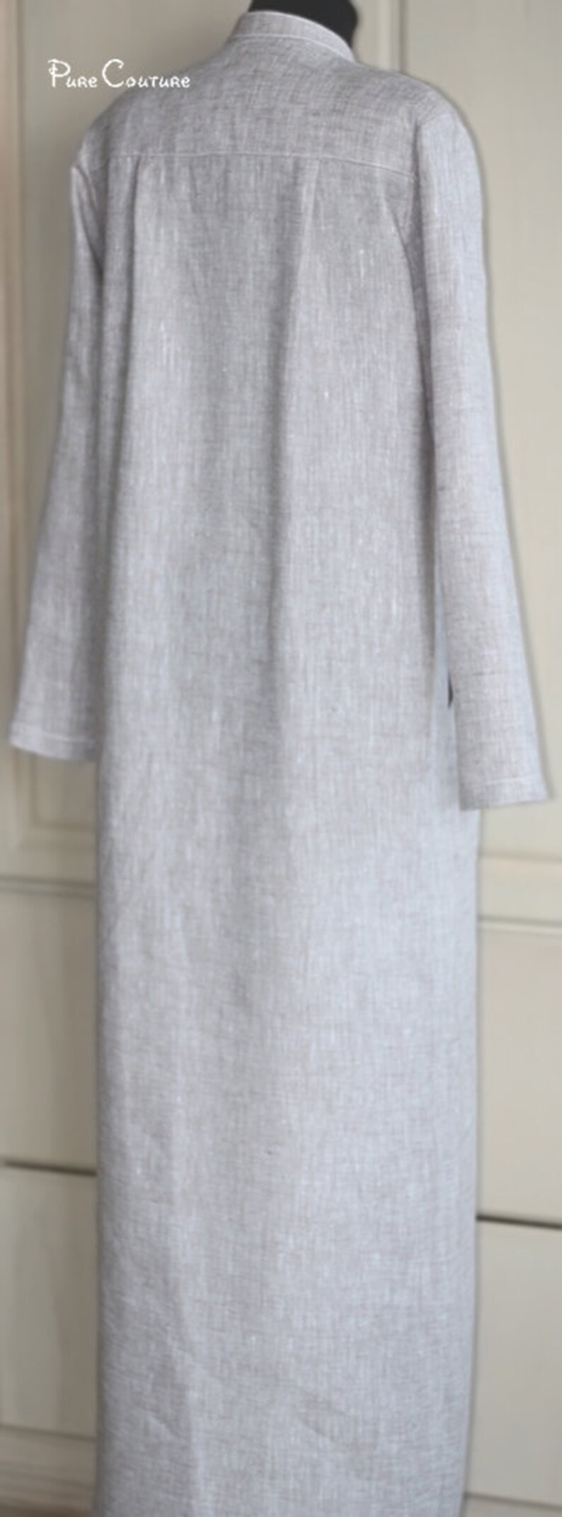 May include: A long, light gray linen shirt with a collar and long sleeves. The shirt has a subtle texture and a relaxed fit.