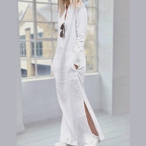 May include: A white long-sleeved maxi dress with a V-neckline and a side slit. The dress has a relaxed fit and is made of a lightweight fabric.