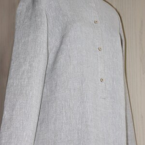 May include: A gray linen shirt with a mandarin collar and a button-up front. The shirt has a relaxed fit and long sleeves.