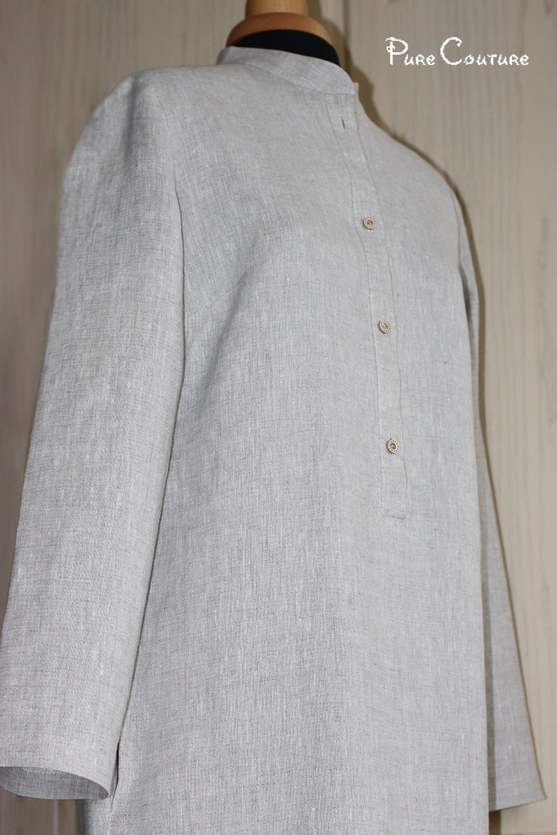 May include: A gray linen shirt with a mandarin collar and a button-up front. The shirt has a relaxed fit and long sleeves.
